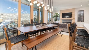 A modern dining area with a long wooden table, black cushioned chairs, and a fireplace. - New Remodel Old Town House by InvitedHome | Walk to Town, Ski, Hot Tub, Patio (Park City)