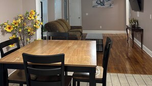 Un coin repas avec une table et des chaises en bois, un ventilateur de plafond et un téléviseur fixé au mur.