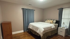 Une chambre à coucher avec un lit, une table de chevet, une armoire en bois et une fenêtre avec des rideaux.