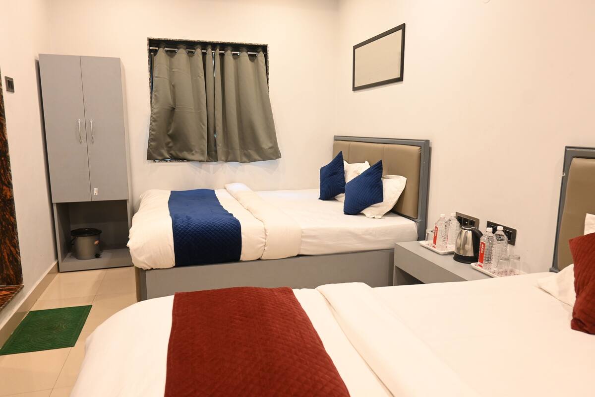 A hotel room with a bed, a wardrobe, a nightstand with a kettle, and a window with curtains.
