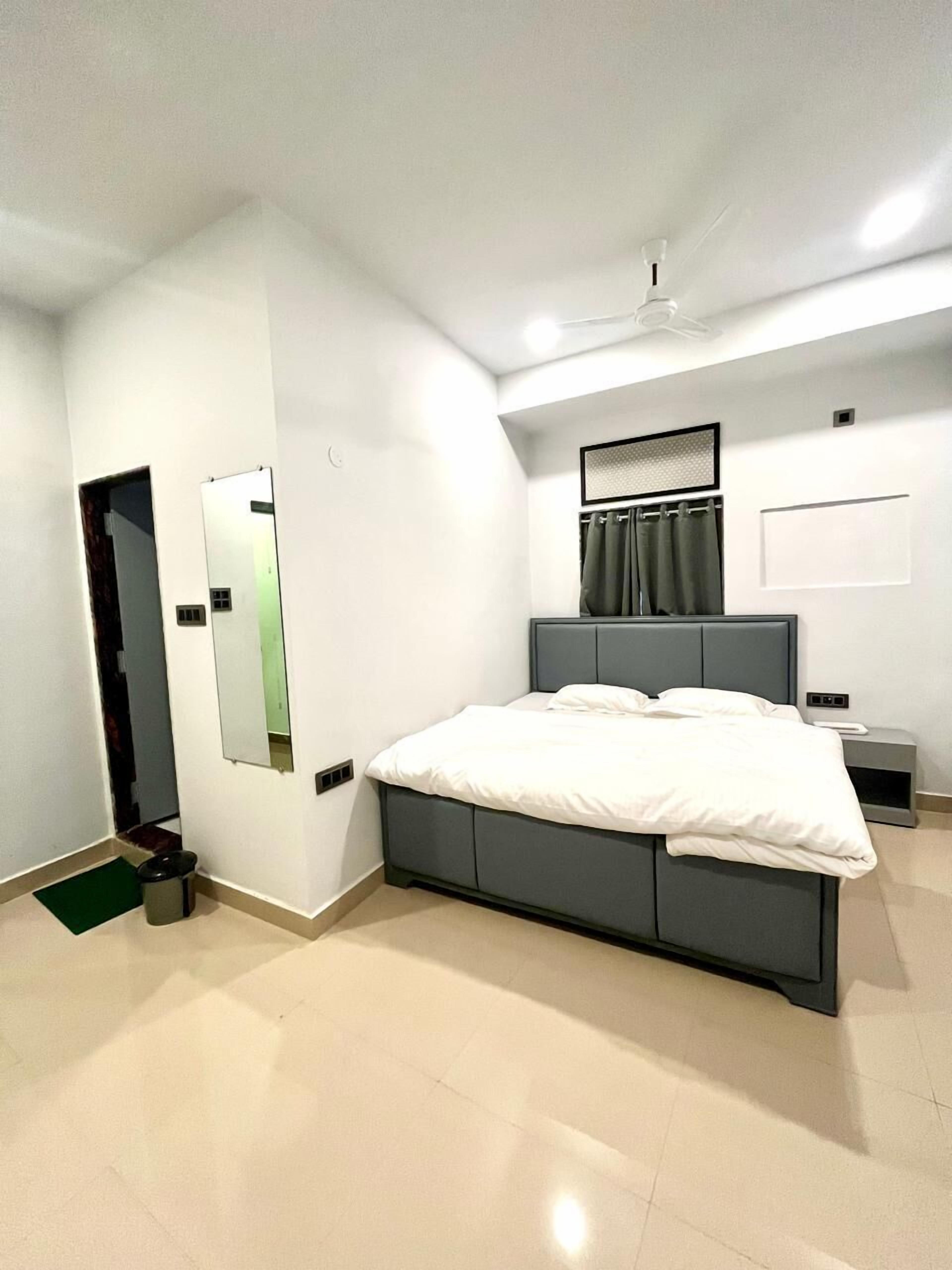 A modern bedroom with a bed, a bedside table, a mirror, a ceiling fan, and a door.