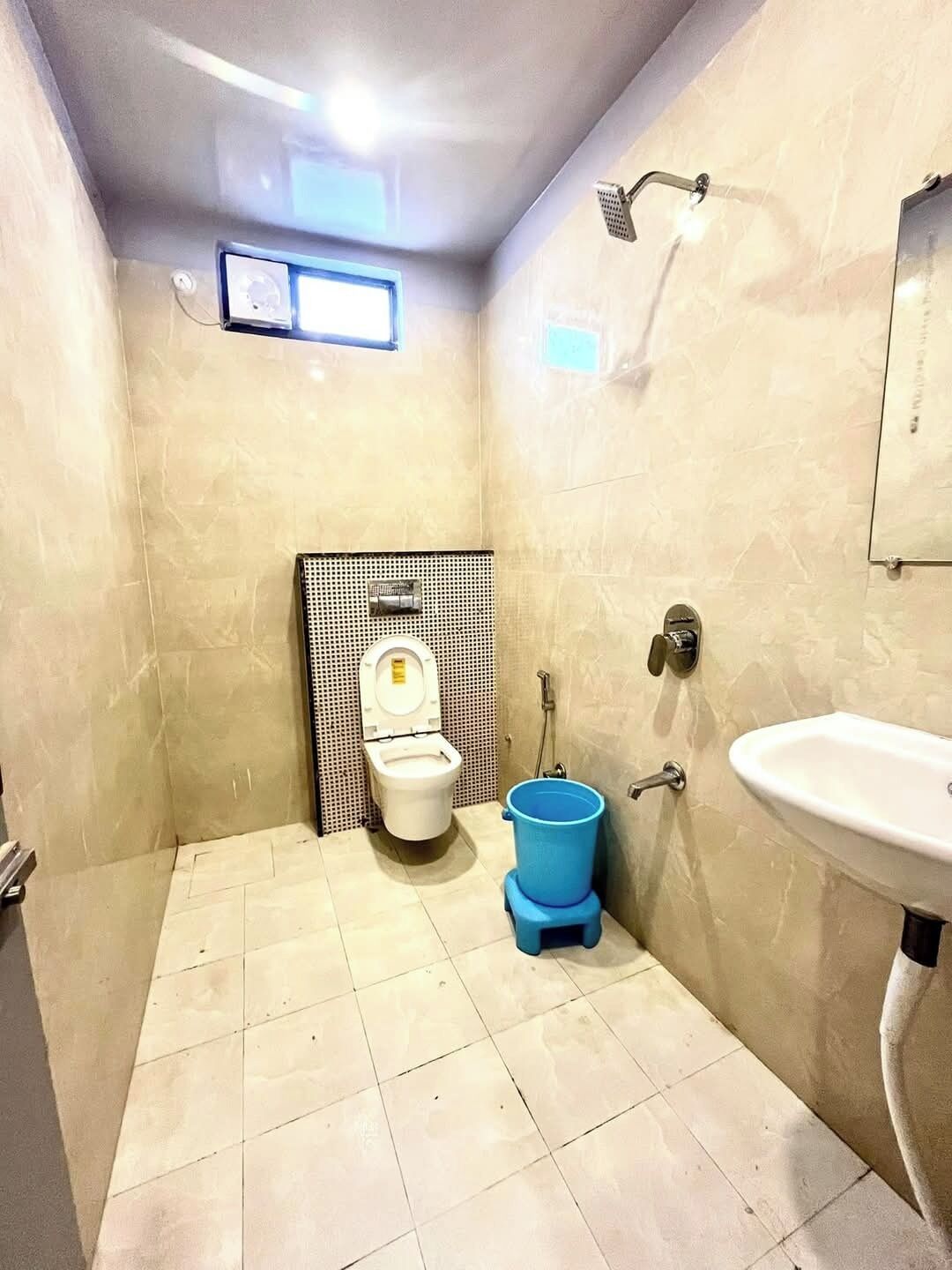 Ein kleines Badezimmer mit Toilette, einem blauen Eimer, einem Waschbecken und einem Duschkopf.