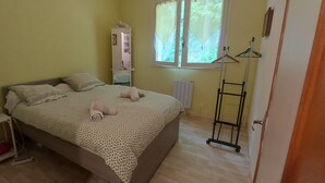 A bedroom with a bed, bedside table, lamp, radiator, window with curtains, and a wardrobe. - Country apartment close to the forest. You can go for a nice walk, (Boussens)