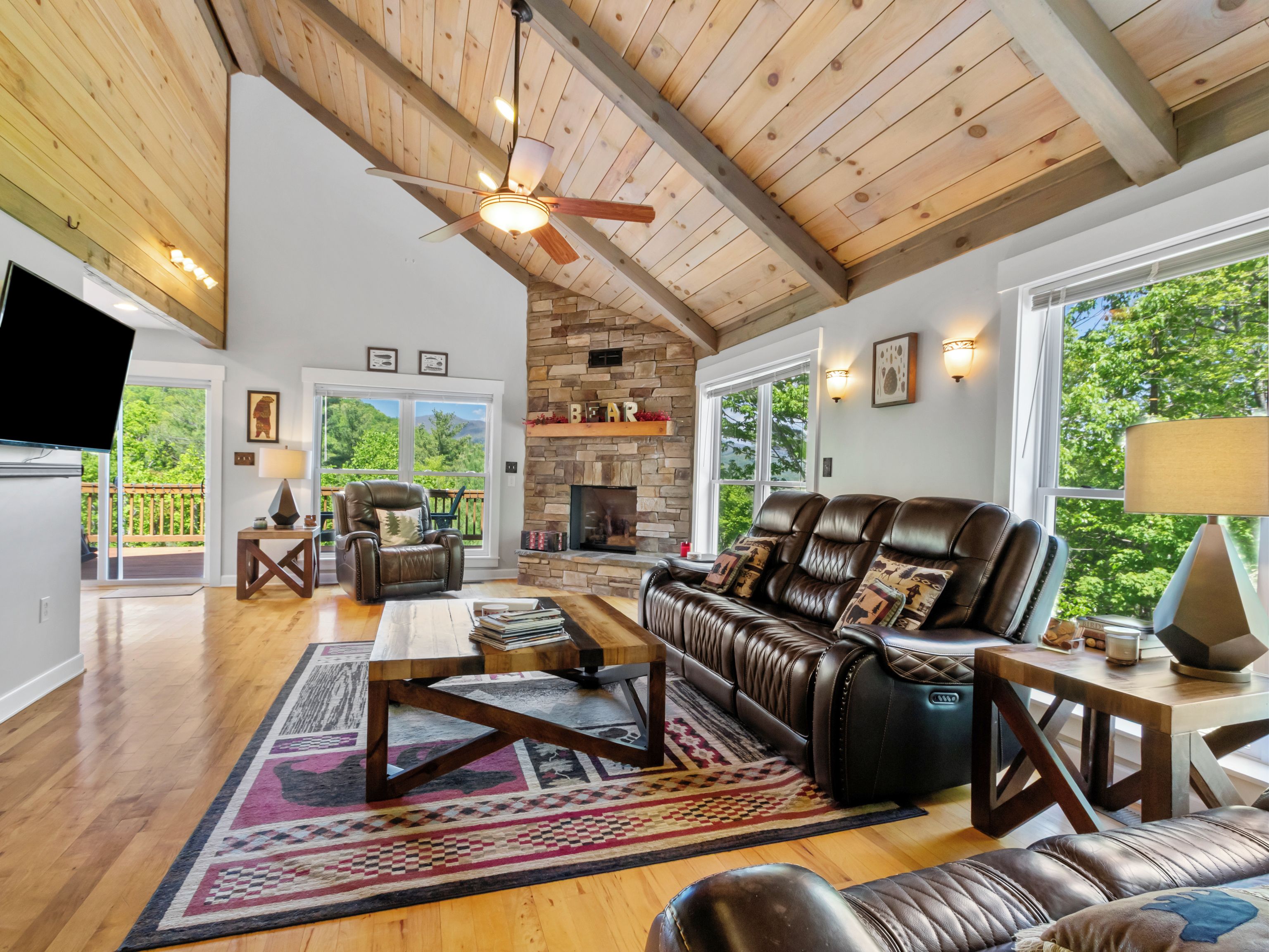A spacious living room with a fireplace, leather furniture, and a large window offering a view of the outdoors.