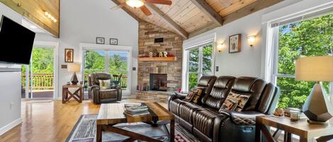 A spacious living room with a fireplace, leather furniture, and a large window offering a view of the outdoors.
