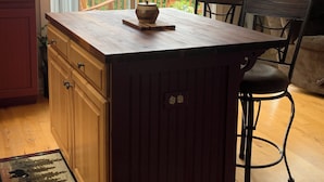 Una cocina con una isla de madera, un comedor con una silla y vistas a montañas a través de ventanas amplias.
