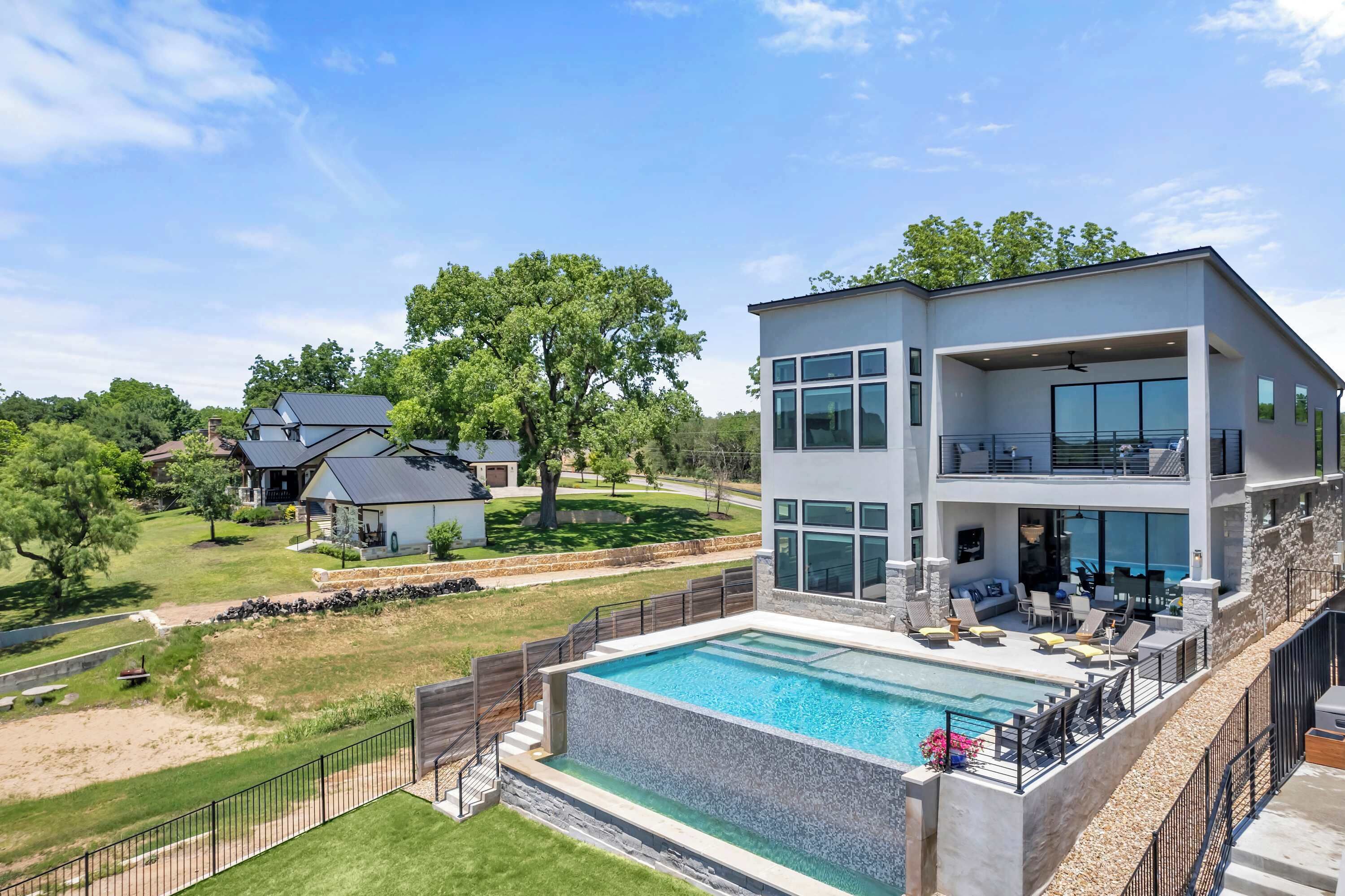 Une maison moderne à deux étages dotée d’une grande piscine, d’un balcon avec coin salon extérieur et d’une vue sur le quartier environnant.