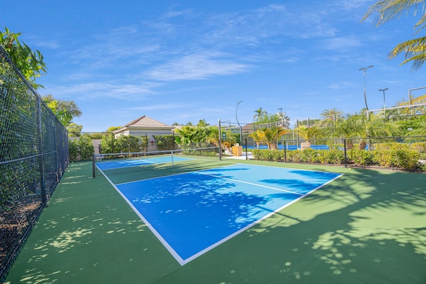 A tennis court with a net, surrounded by a fence, and palm trees in the background. - Aqualina (Nassau)