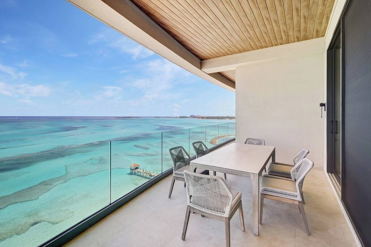 A balcony with a table and chairs overlooking a turquoise sea and a clear sky.