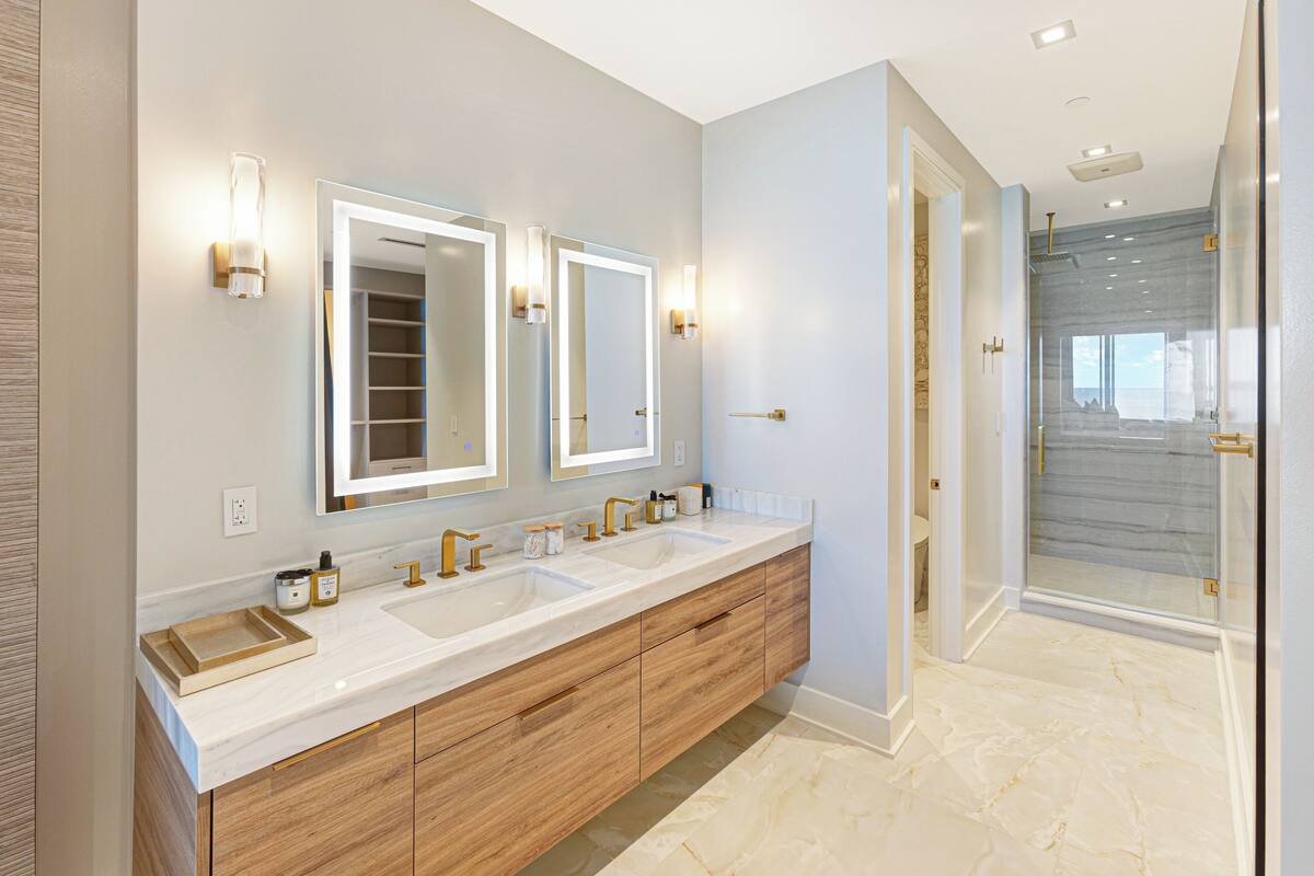 A modern bathroom with a double sink vanity, two wall-mounted mirrors, and a glass shower enclosure.