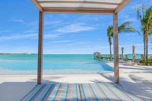 A beachside pool area with lounge chairs and umbrellas, a wooden deck, and a view of the ocean. - Aqualina (Nassau)