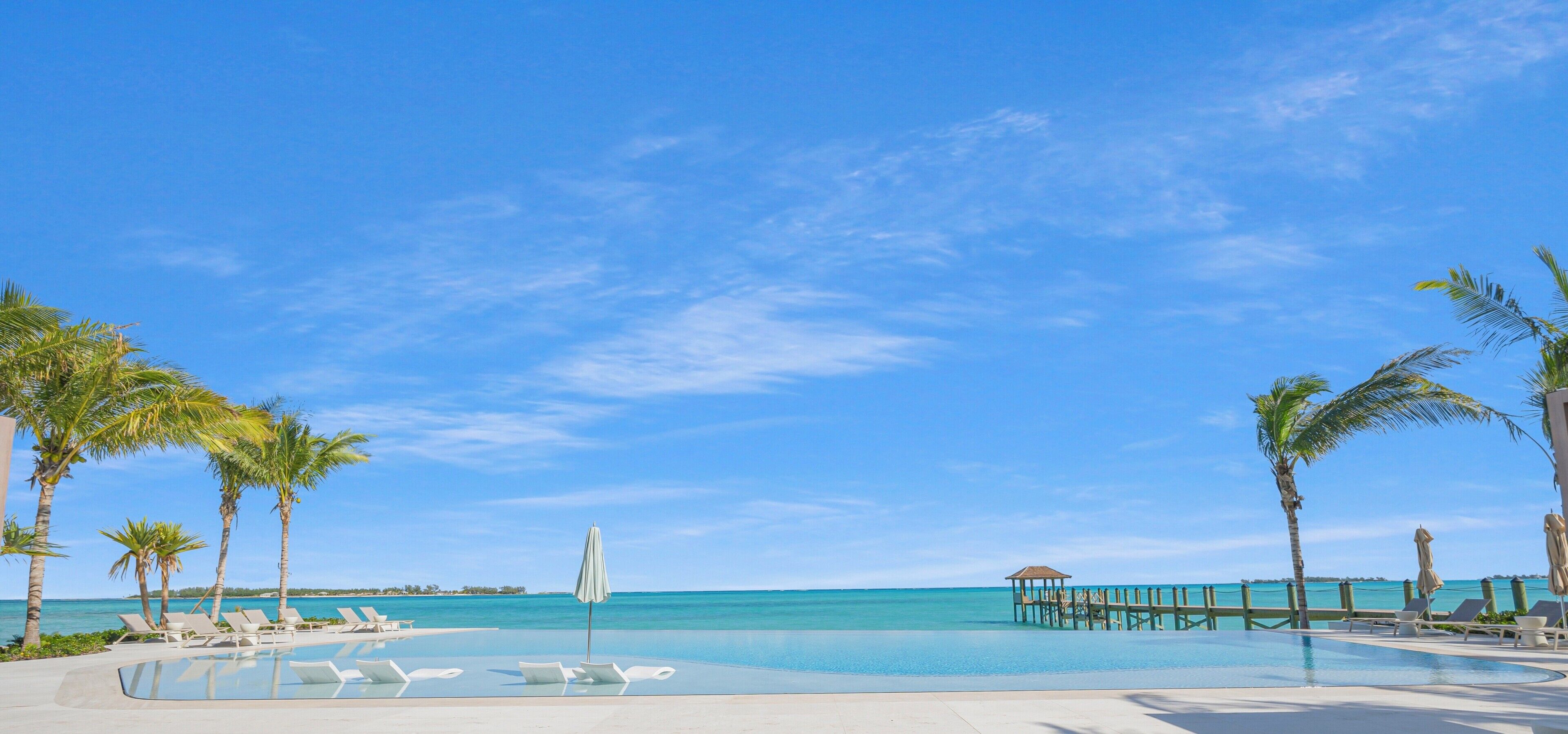 Un ciel d’un bleu éclatant, une piscine bordée de chaises longues, des palmiers et une vue lointaine sur l’océan.