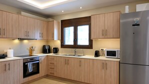 Una cucina moderna con mobili chiari in legno, un frigorifero in acciaio inossidabile, un forno a microonde, un lavello e una finestra sopra il lavello.