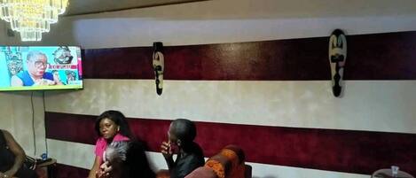 Un bar con una pantalla de televisión mostrando un noticiero, una araña y una pared con rayas horizontales.