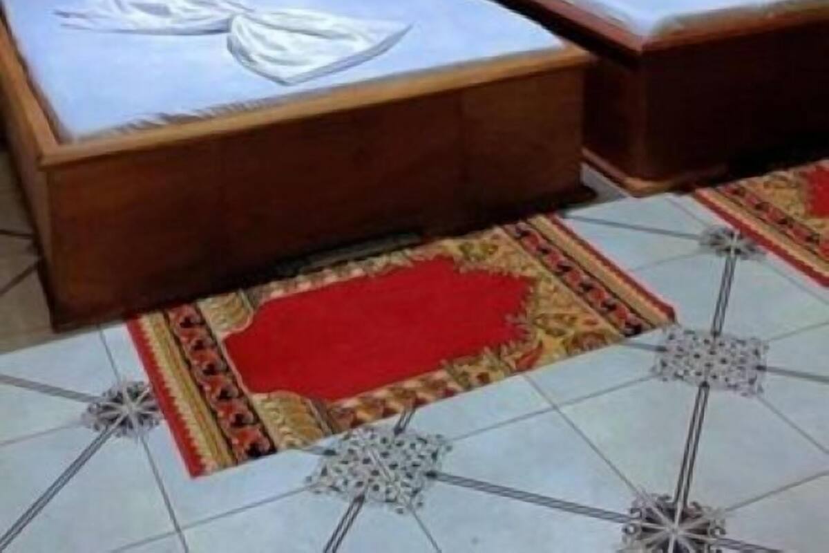 A room with two beds, a window with curtains, a patterned rug, and an air conditioning unit.