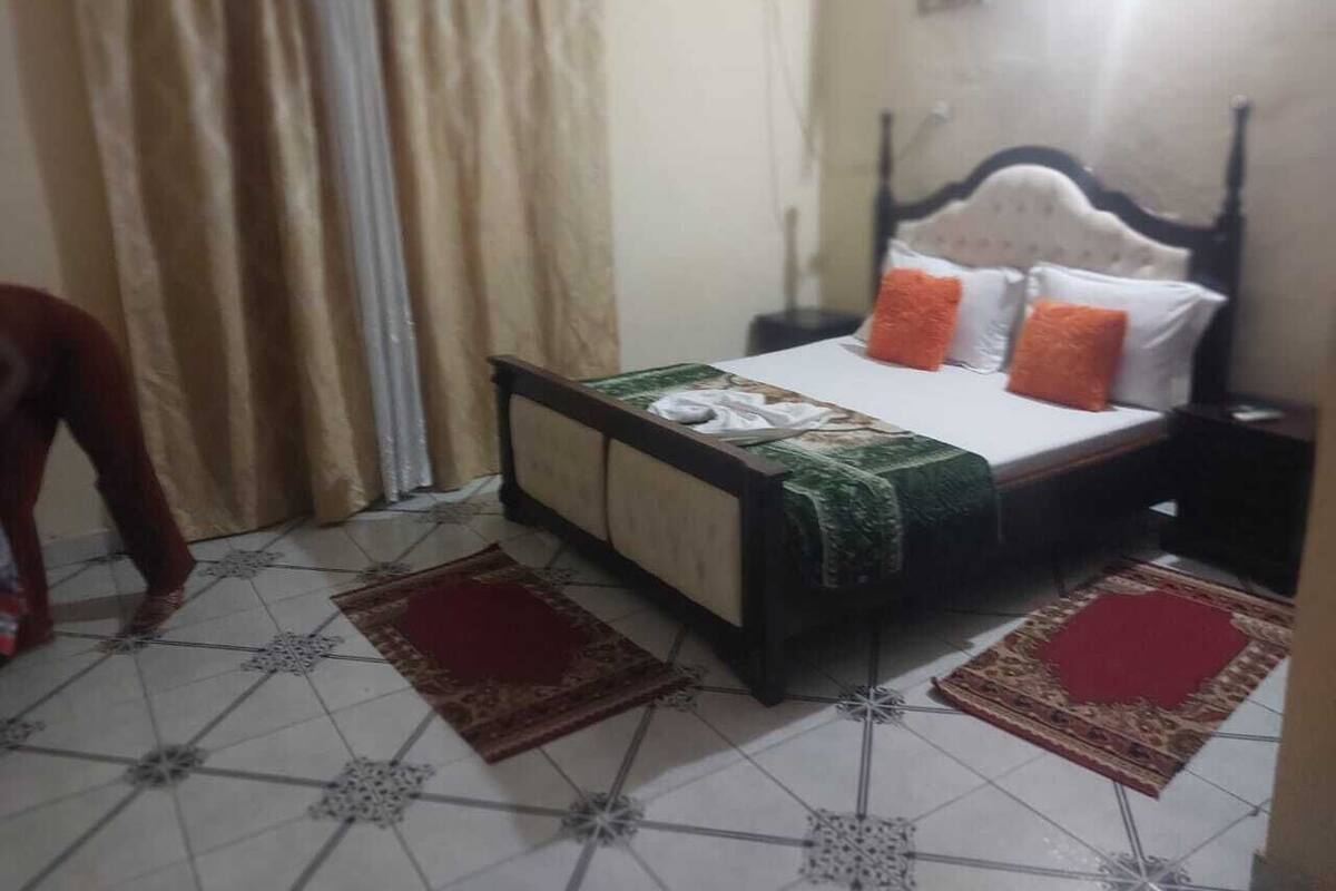 A bedroom with a bed, curtains, a radiator, and a tiled floor.