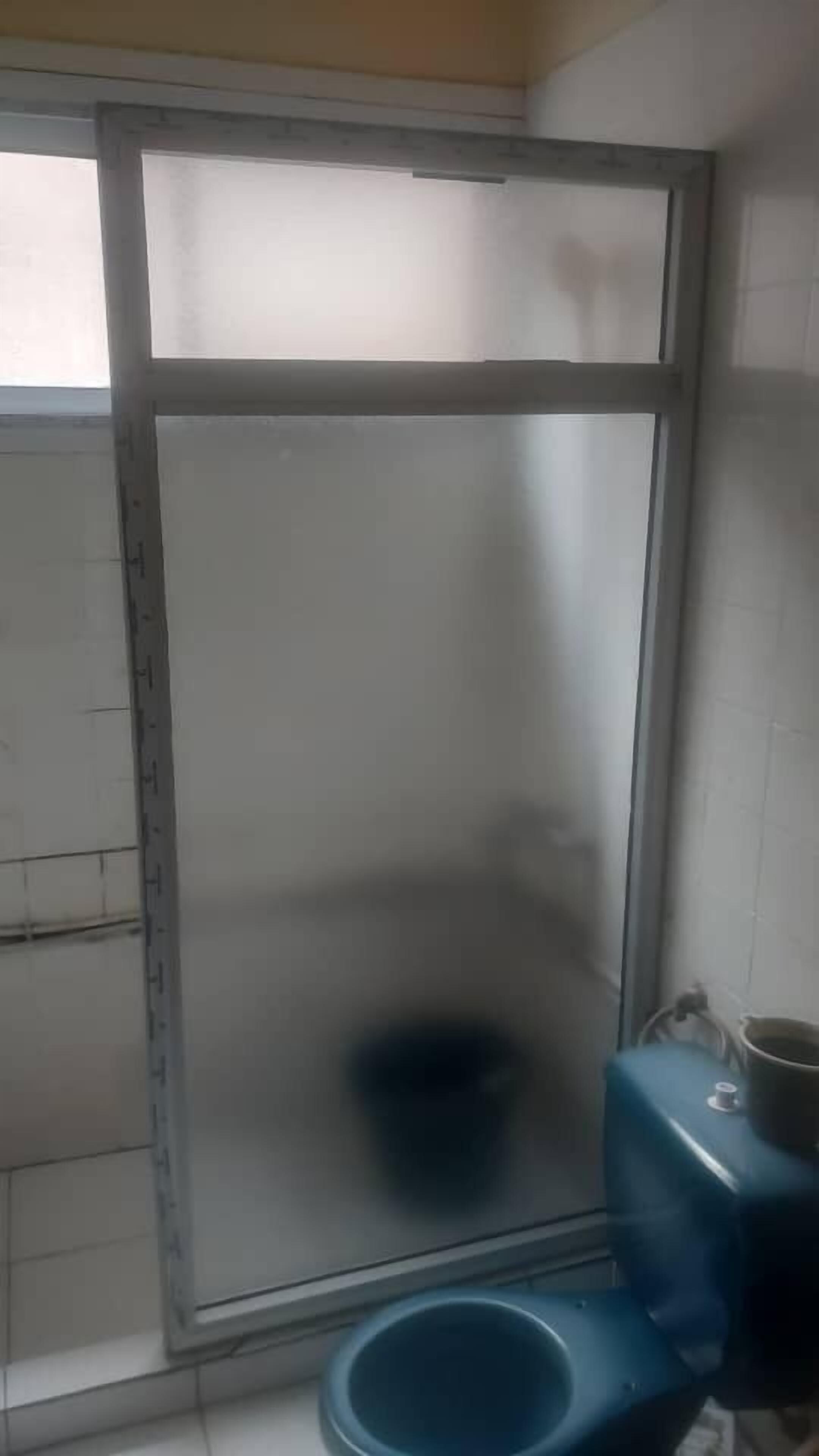 Egy nagy ablakos fürdőszoba, kék WC-vel és egy csészével ellátott mosdókagylóval.