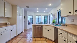 A modern kitchen with white cabinetry, a wooden countertop, and a view of the garden through large windows.