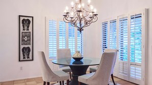 A dining area with a glass table, four chairs, a chandelier, and a patterned rug.