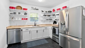 Una cocina moderna con armarios blancos, electrodomésticos de acero inoxidable y utensilios de cocina en rojo y negro sobre estantes.