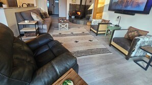 A cozy living room with a fireplace, leather sofas, and a television mounted on the wall. - Welcome to Cozy Doo's Casa -A Warm, Woodsy Getaway in Angel Fire, NM (Angel Fire)