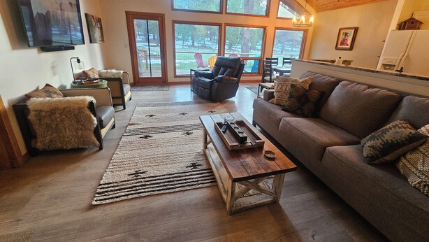 A spacious living room with a large window, a sofa, a coffee table, and a fireplace. - Welcome to Cozy Doo's Casa -A Warm, Woodsy Getaway in Angel Fire, NM (Angel Fire)
