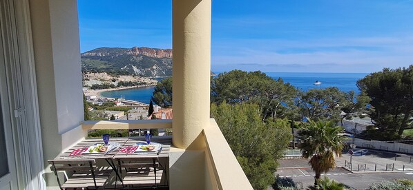 A balcony with a table set for dining, overlooking a coastal landscape with cliffs and a beach.