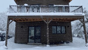 Una cabaña de madera de dos pisos con un balcón, rodeada de nieve.