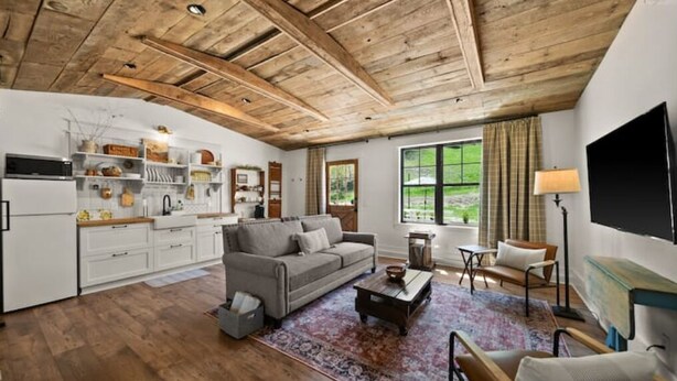 A spacious living area with a wooden ceiling, a grey sofa, a coffee table, and a TV.
