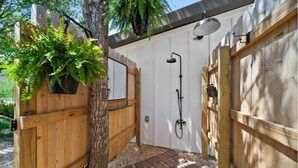 A wooden gate with a potted plant, a white door, and a shower area with a hose.