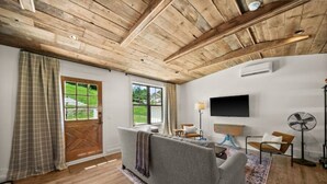A living room with a wooden ceiling, a sofa, a TV, a fan, and a door leading outside.