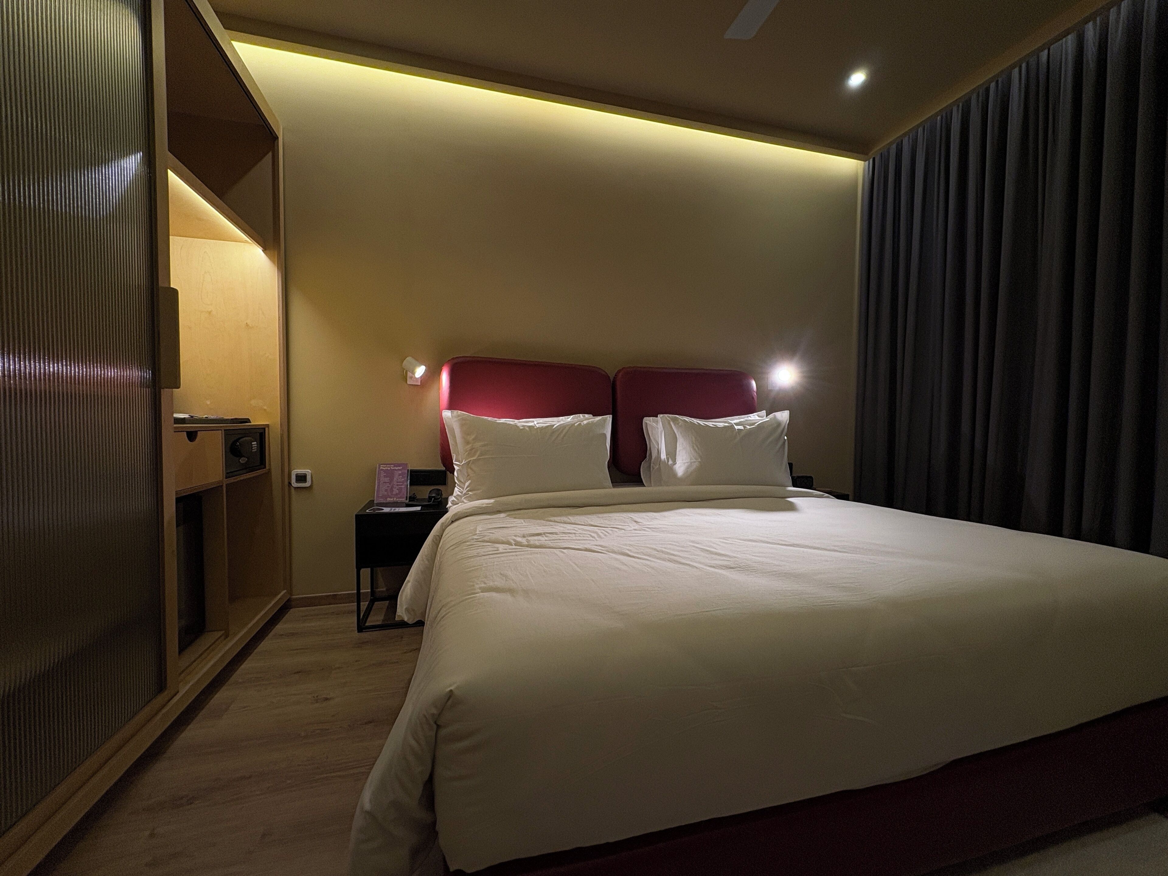 A hotel room with a large bed, a nightstand, a wall-mounted lamp, and a sliding door.