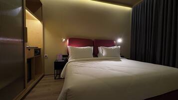 A hotel room with a large bed, a nightstand, a wall-mounted lamp, and a sliding door.