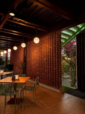 Interior de restaurante con paredes de ladrillo, lámparas colgantes y vistas a una escalera verde y flores.