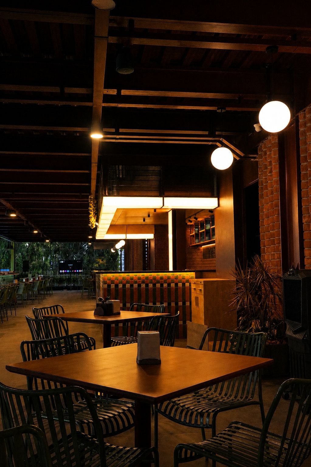 An indoor dining area with tables and chairs, a bar area with stools, and a brick wall.