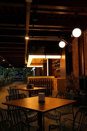An indoor dining area with tables and chairs, a bar area with stools, and a brick wall.