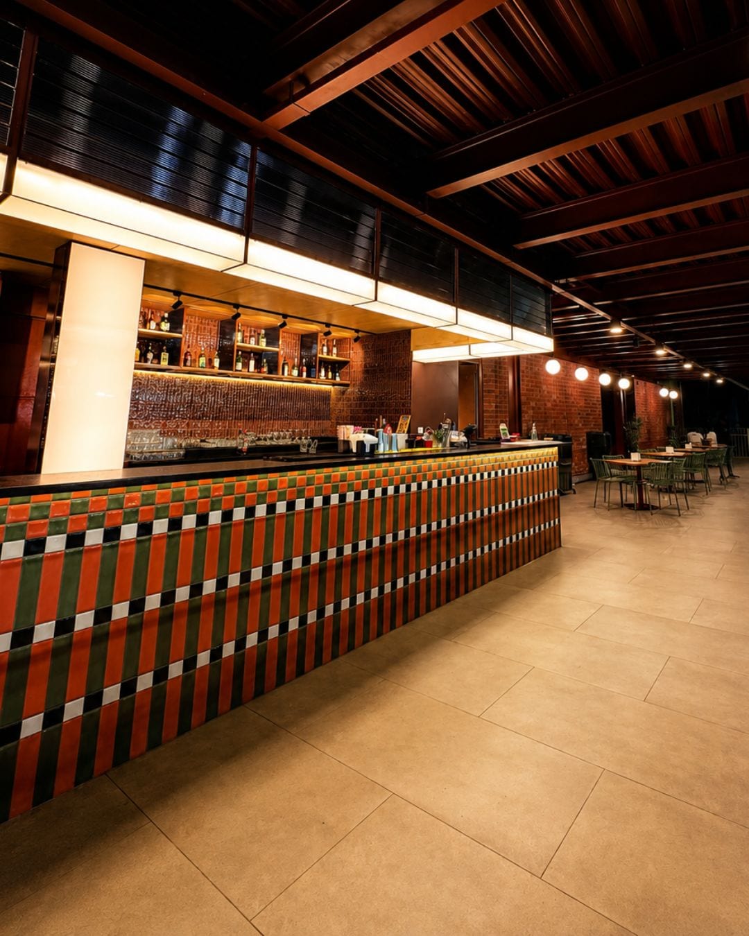 A bar area with a tiled counter, shelves with bottles, and a seating area with tables and chairs.