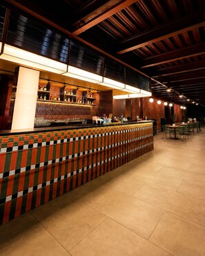 Zona de bar con mostrador de baldosas, estanterías con botellas y un área de estar con mesas y sillas.