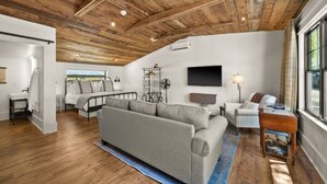 Un salon spacieux avec un plafond en bois, un canapé gris, une petite table et une grande fenêtre.