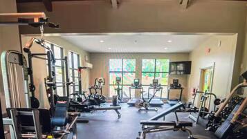A gym with various exercise equipment, large windows, and a ceiling with exposed beams.