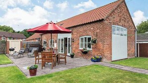 Una casa de ladrillo con techo de tejas, un patio con mobiliario exterior y una sombrilla roja.