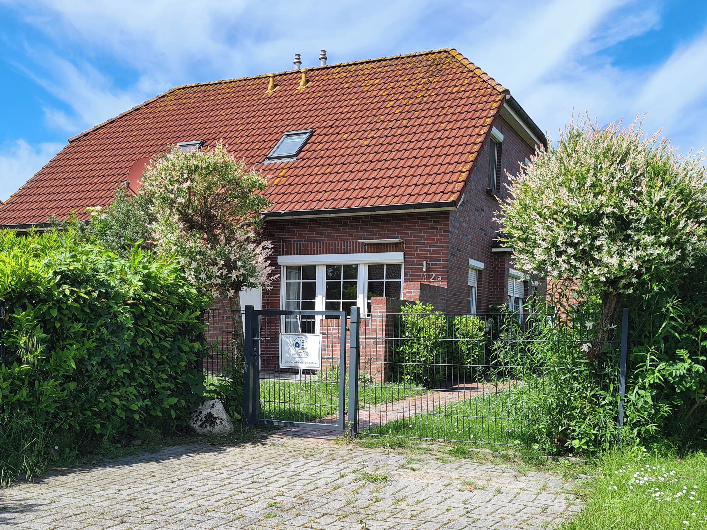 Une maison en briques avec un toit recouvert de tuiles rouges, une entrée avec portail et une allée pavée.
