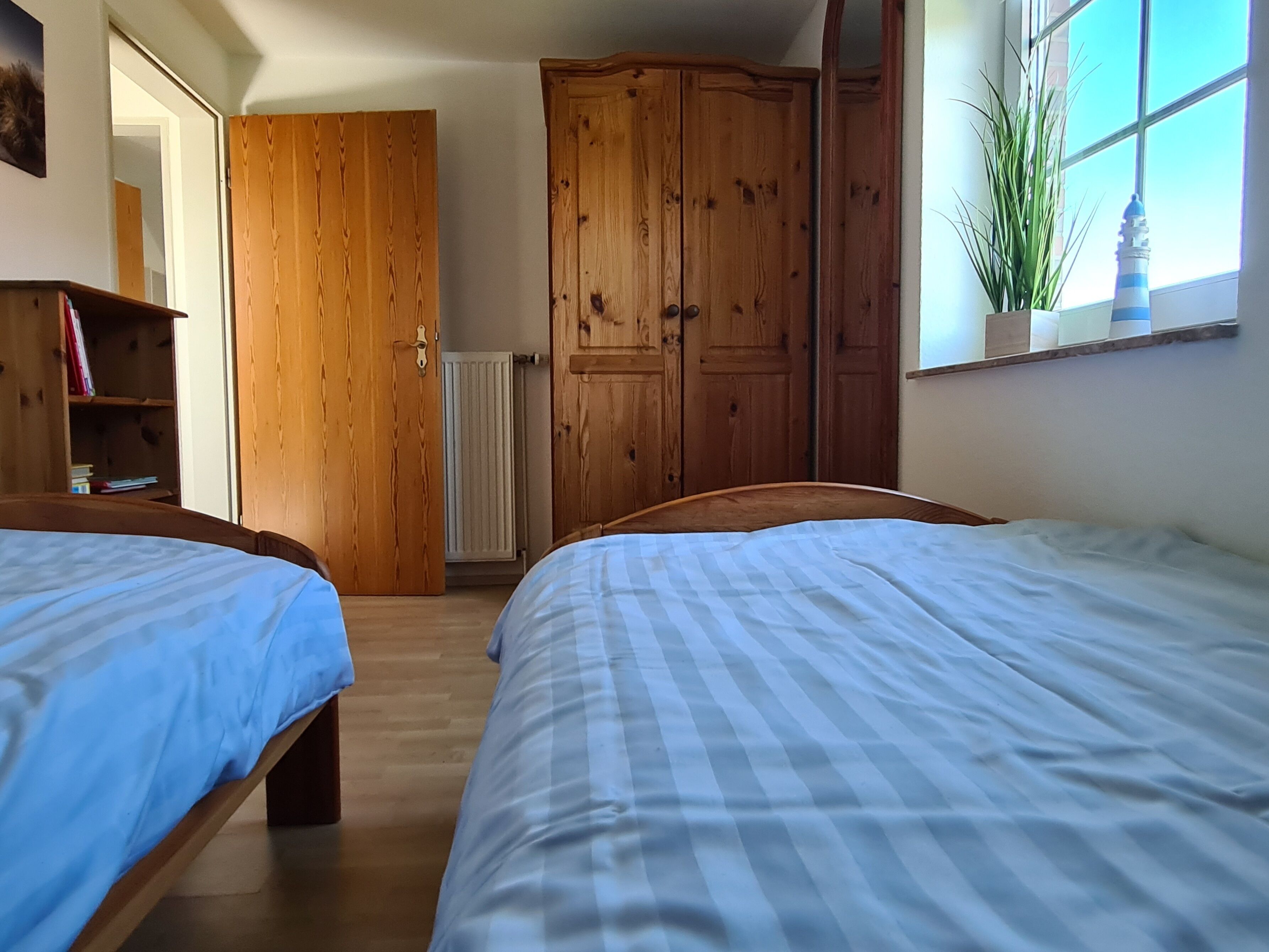 A bedroom with two beds, wooden wardrobe, a radiator, and a window with a plant.