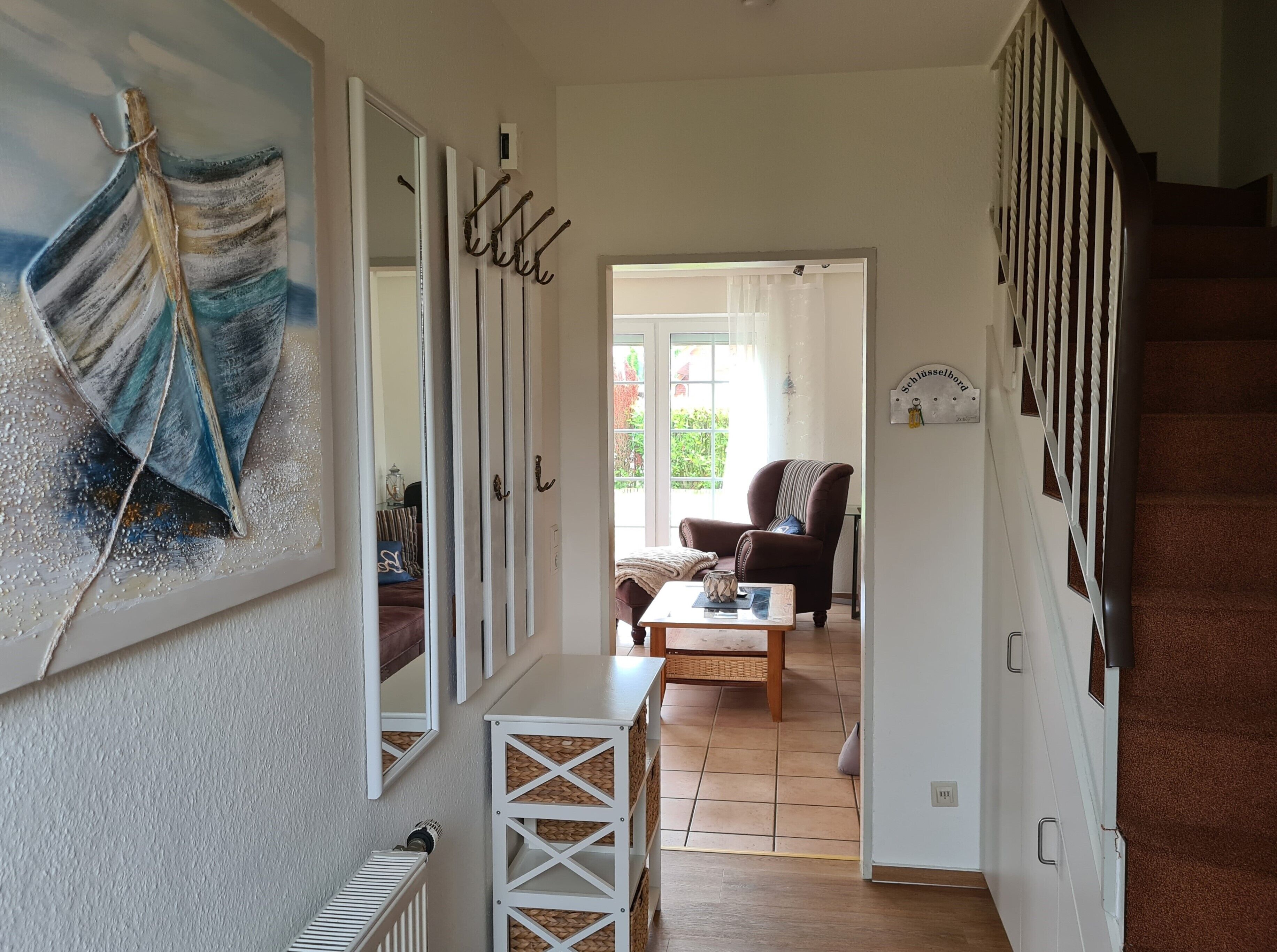 Ein Flur mit einer Spiegelwand, einer Holzkiste und Blick in ein Wohnzimmer mit Sofa und Sessel.