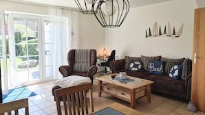 Una sala de estar con un sofá marrón, un sillón a rayas, una mesa de centro de madera y un comedor con mesa y sillas.