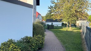 Un quartier résidentiel avec un chemin pavé, une cour bordée d’arbres et un bâtiment blanc surmonté d’un toit rouge.