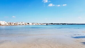 A beach with a clear sky, sandy shore, and buildings in the background. - Charming Italian Villa in Torre Castiglione With Private Entrance (Porto Cesareo)