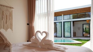 A bedroom with a bed, a macrame wall hanging, and a view of a swimming pool.