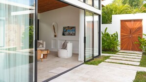 A modern house with a glass door leading to a living area with a white sofa and a round wooden table.