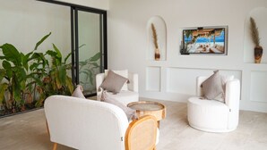 A modern living room with a sofa, two armchairs, a coffee table, and a television on the wall.